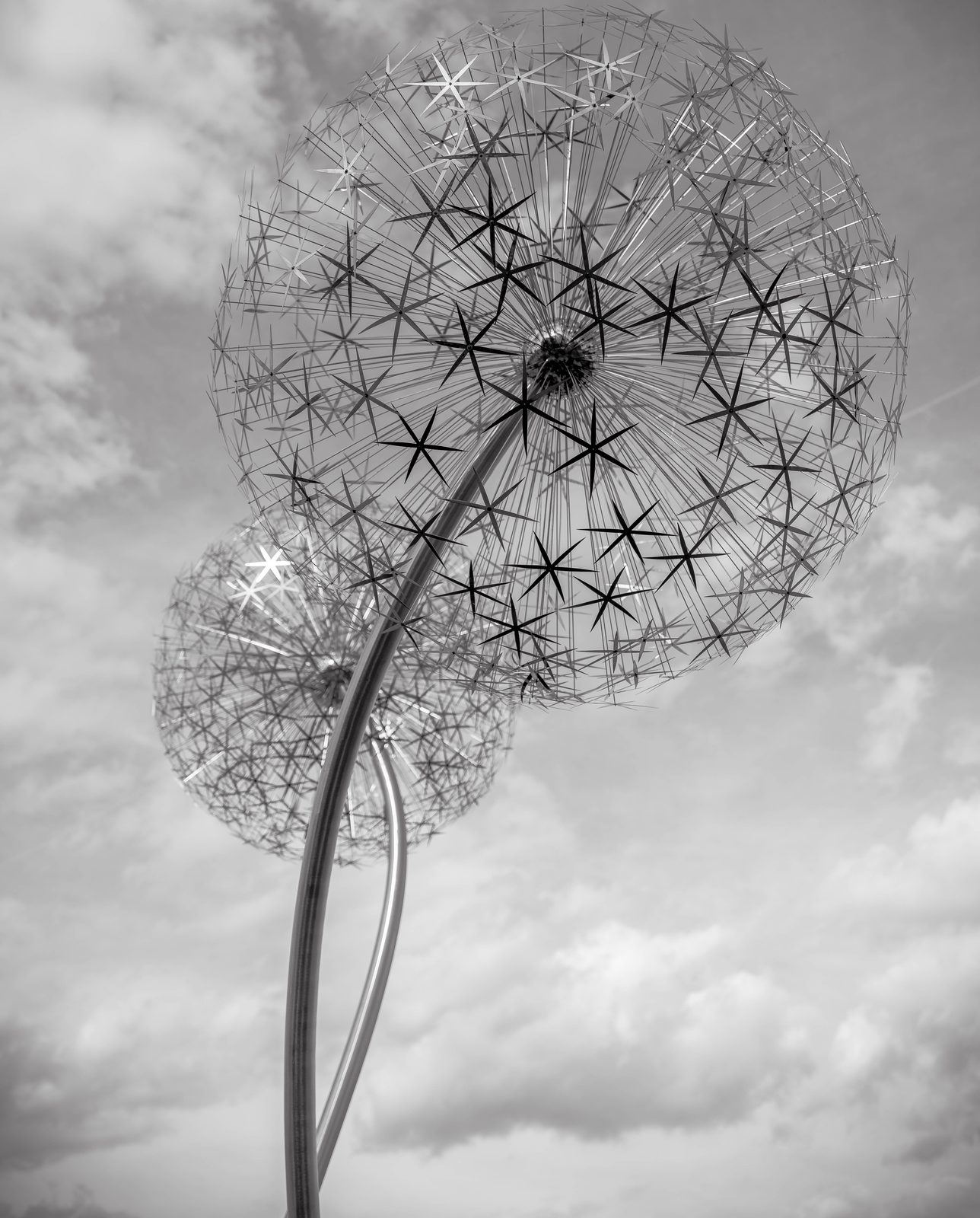Dandelion seed-head sculpture against a cloudy sky, black and white